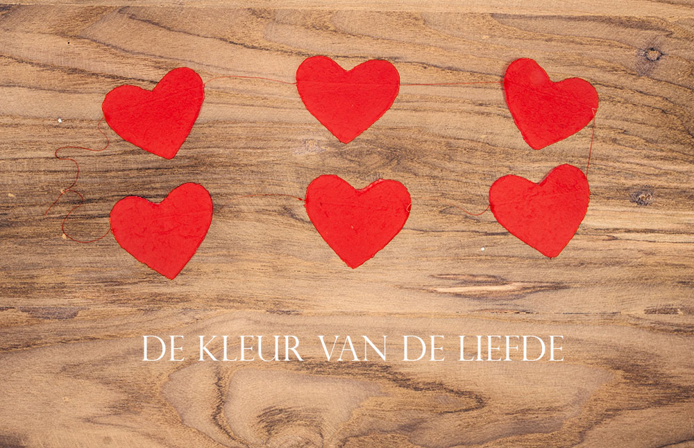 Een houten achtergrond met daarop een slinger van 2,2 meter met 6 rode hartjes van moerbijschors en de tekst 'de kleur van de liefde'